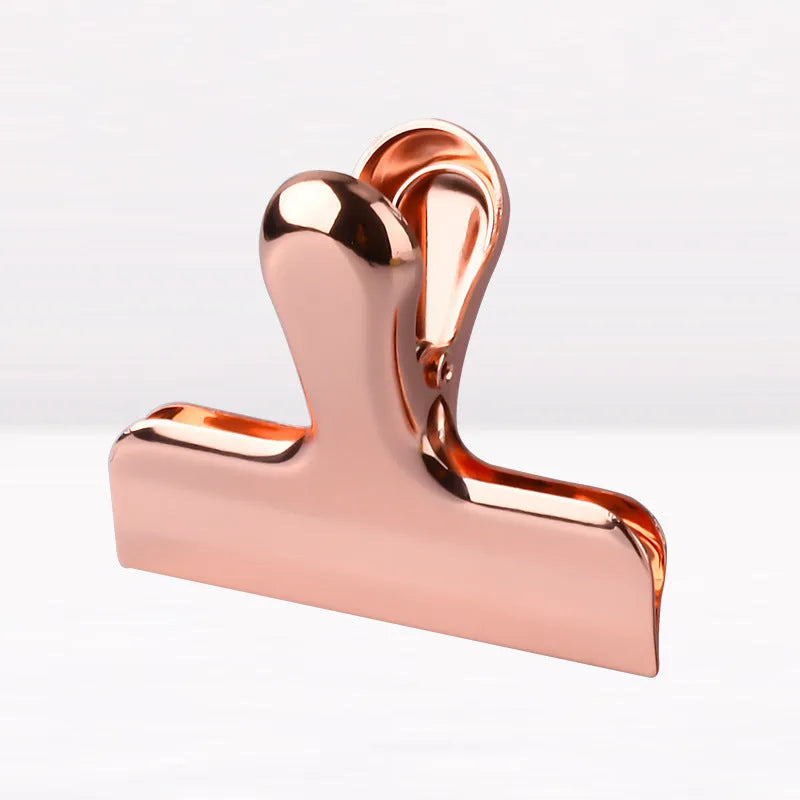 Gold stainless steel dovetail clip holding a stack of papers on a desk