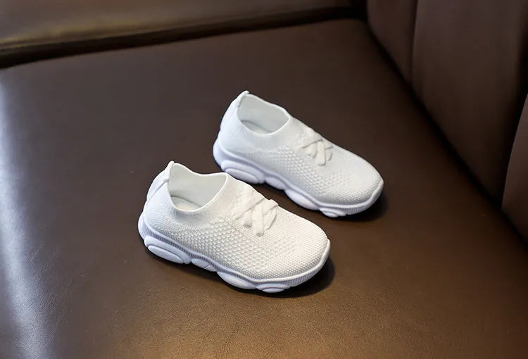 Children's white fabric lazy slip-on shoe with a non-slip rubber sole on a wooden floor.