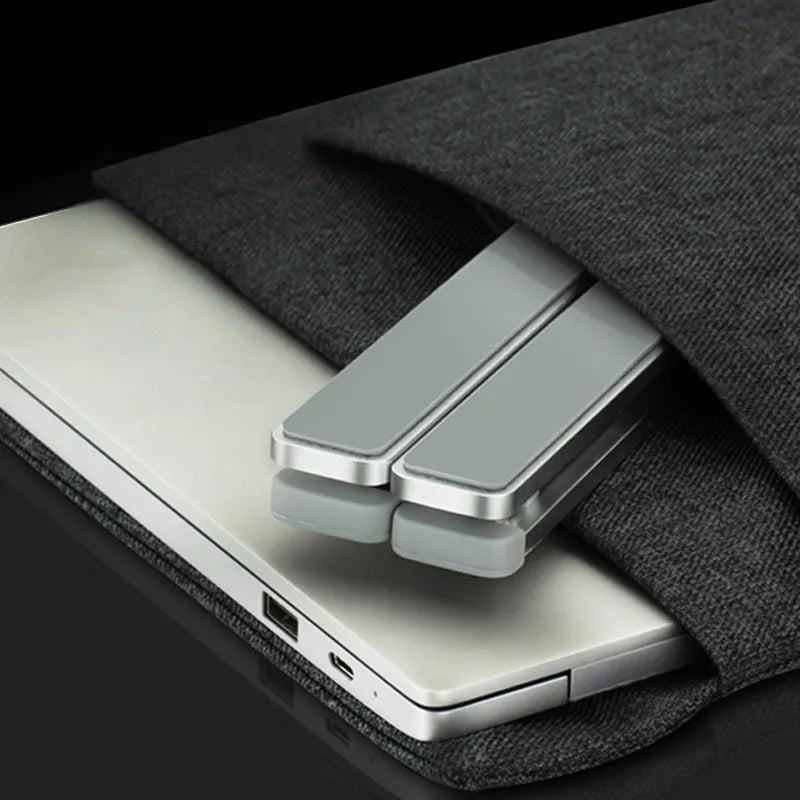 Silver adjustable folding laptop stand with hollow bottom and non-slip pads on a desk