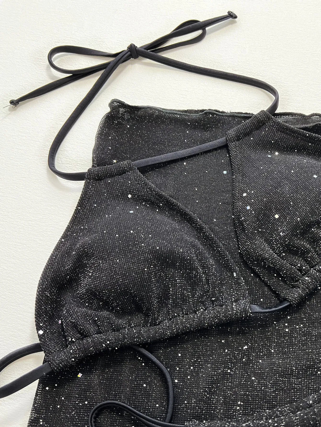 Black three-piece bikini swimsuit set with top and shorts on a plain background.