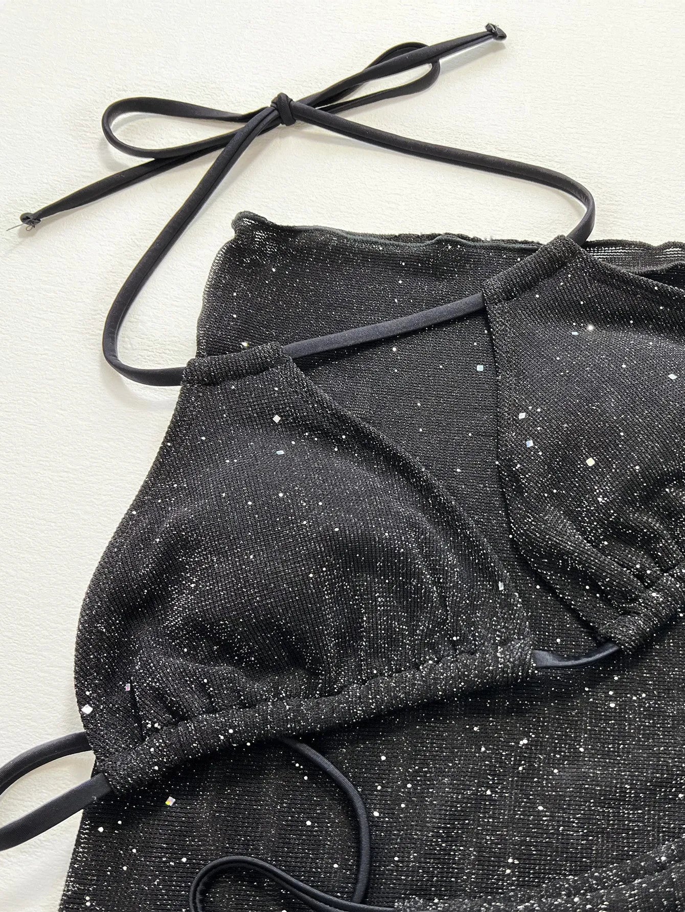 Black three-piece bikini swimsuit set with top and shorts on a plain background.