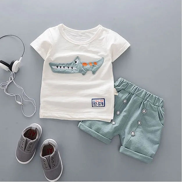 Baby boy wearing a blue crocodile print cotton t-shirt and matching blue shorts summer outfit set.