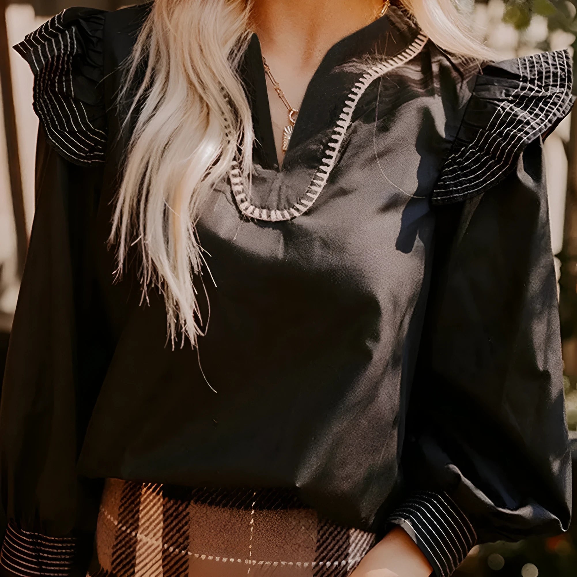 Black women's V-neck blouse with long ruffle sleeves and contrast white stitching on seams.