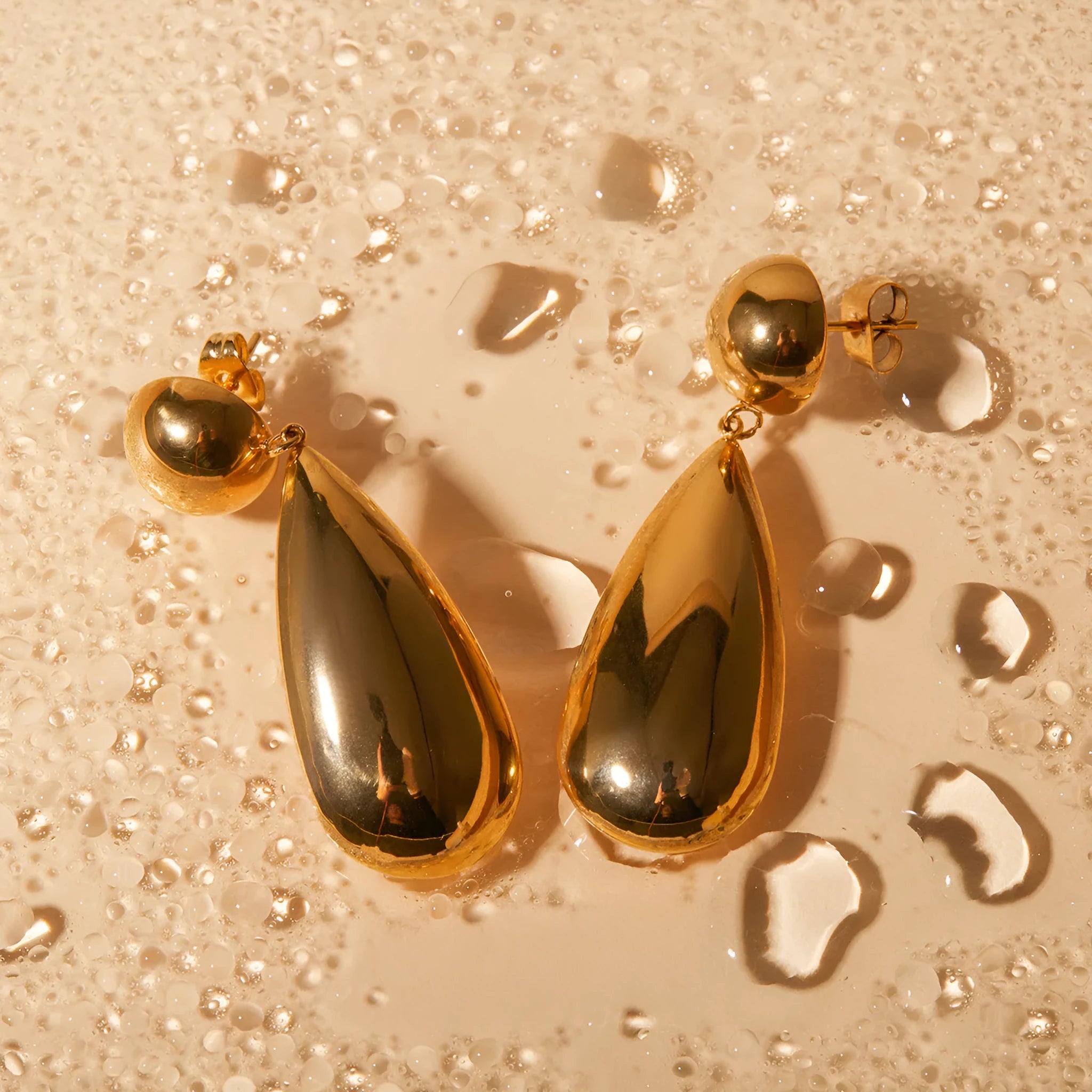 Gold coloured stainless steel earrings with a geometric hemisphere and water drop pendant design.