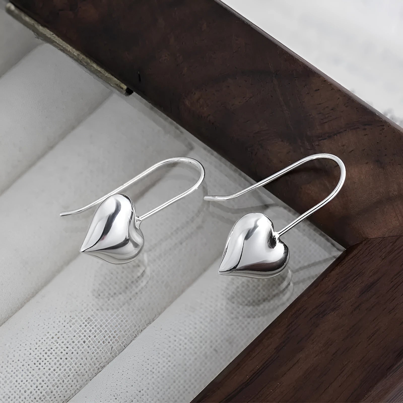 Silver coloured heart-shaped earrings with three-dimensional design and ear hooks