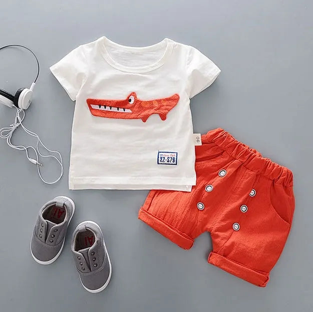Baby boy wearing a blue crocodile print cotton t-shirt and matching blue shorts summer outfit set.