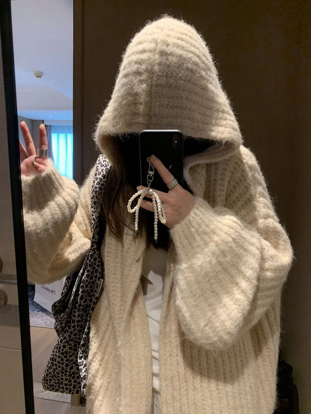 A woman wearing a thick, loose-fit, dark grey hooded sweater cardigan with a retro design.