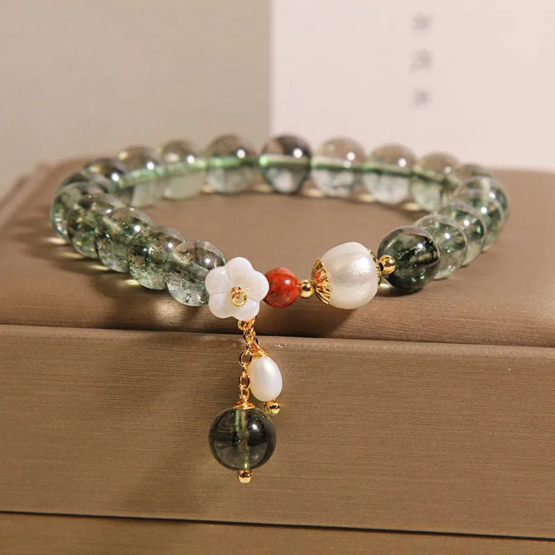 Green phantom quartz crystal bracelet with shell flower charm on a woman's wrist