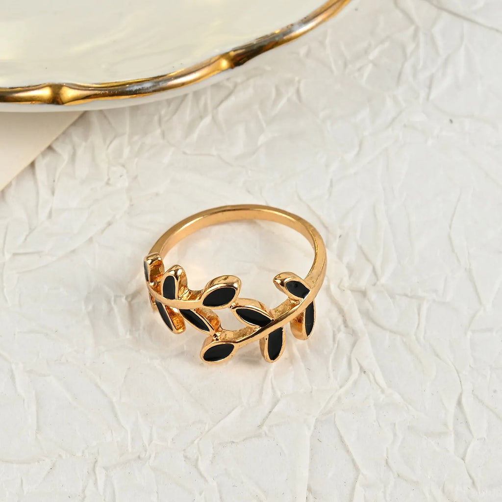Gold-coloured acrylic ring with a geometric leaf and floral design on a white background.