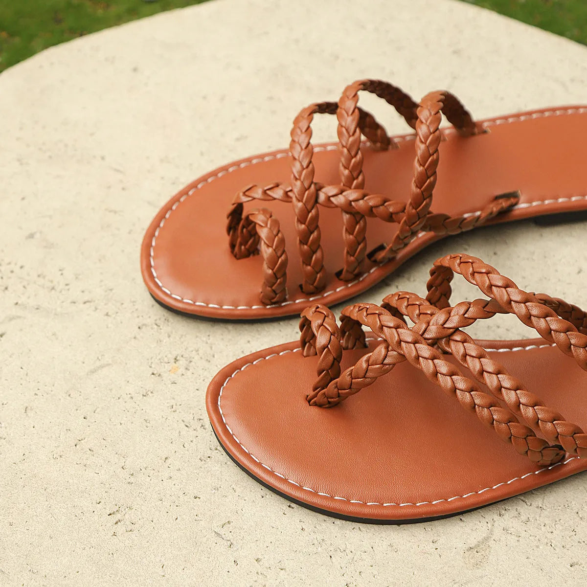 Women's brown woven clip-toe flat sandals on a light background.