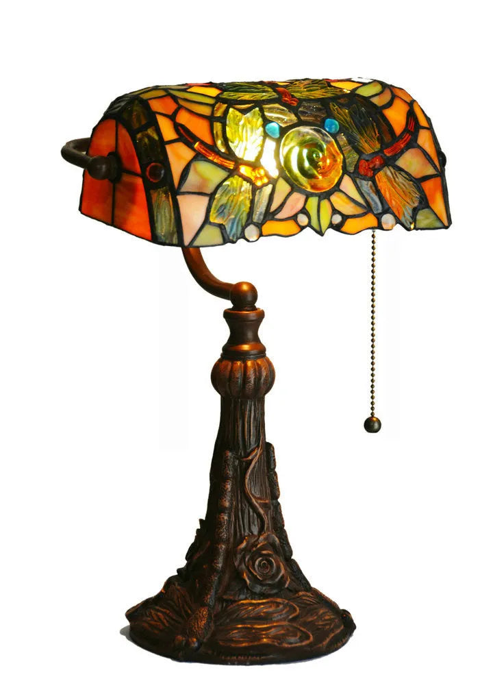 Tiffany-style desk lamp with coloured stained glass shade and resin base on a wooden desk.