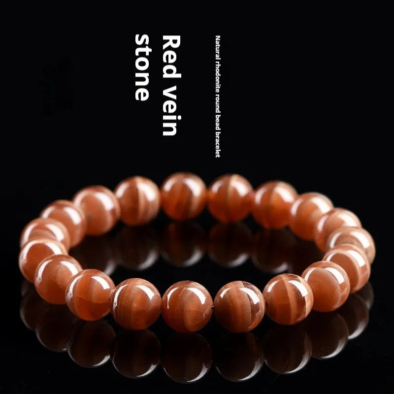 Natural old mine rhodochrosite round bead bracelet with geometric and Ruyi design on a wrist.