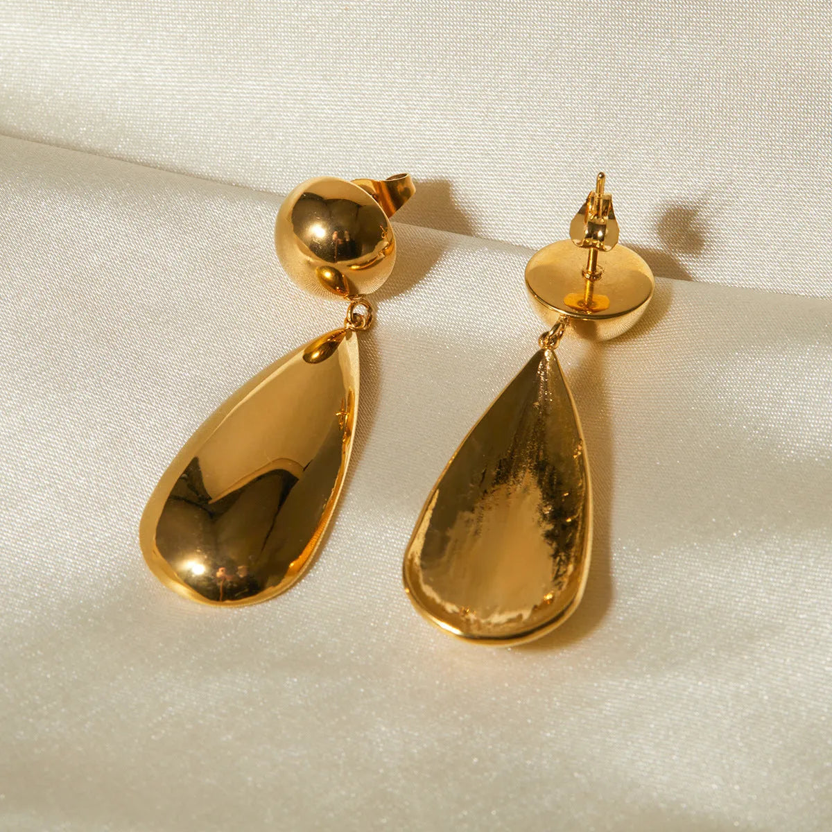Gold coloured stainless steel earrings with a geometric hemisphere and water drop pendant design.