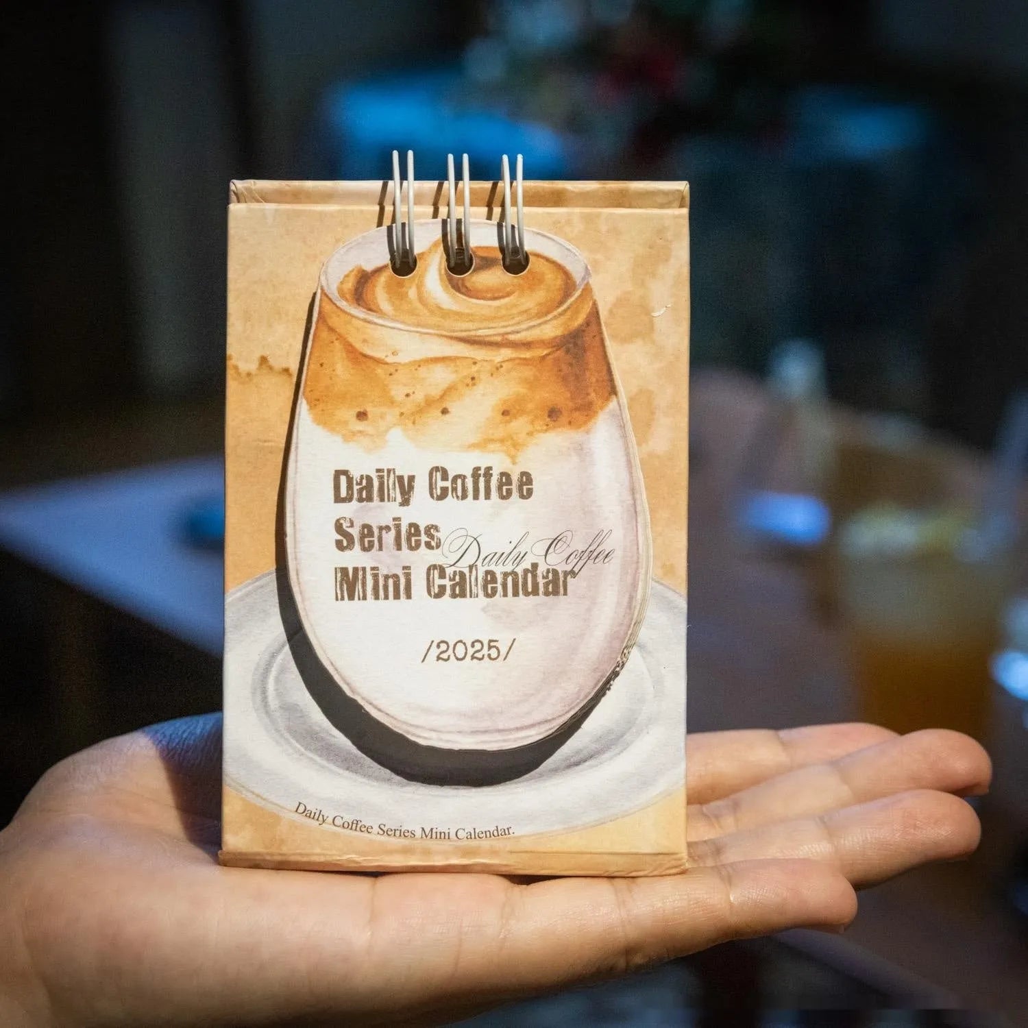 Small 2025 mini desk calendar open to a daily page, showing modern simple design on a desk.