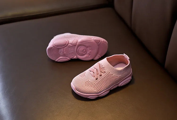 Children's white fabric lazy slip-on shoe with a non-slip rubber sole on a wooden floor.