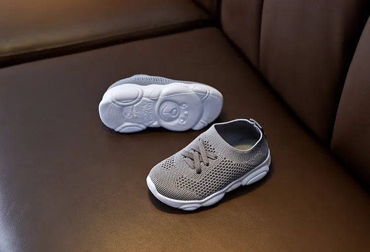 Children's white fabric lazy slip-on shoe with a non-slip rubber sole on a wooden floor.