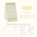 Cream coil-bound desk calendar for 2022, paper, Regular size, on a desk with month view visible