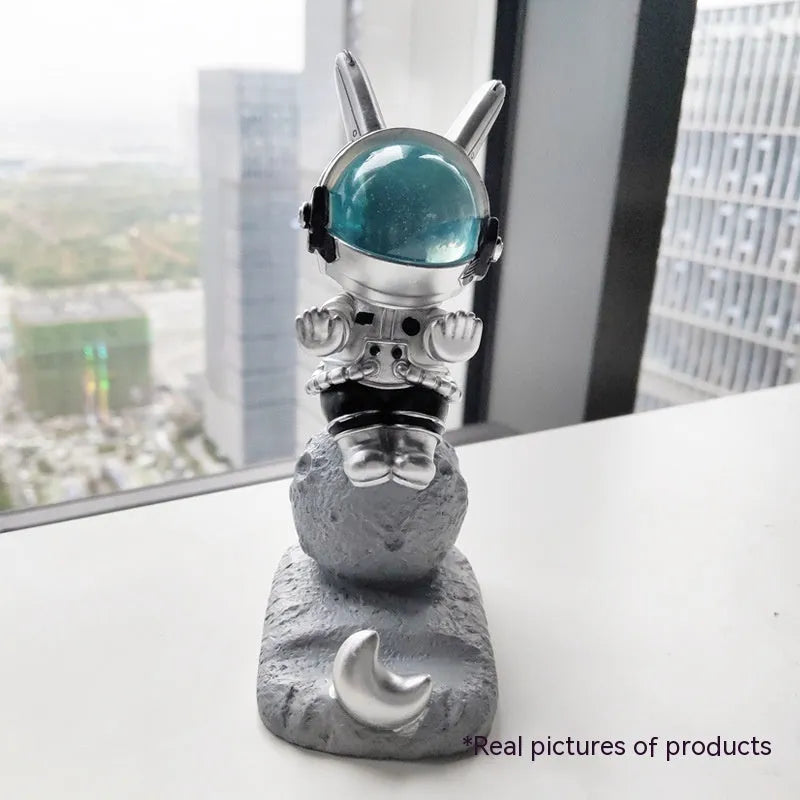Space Rabbit resin phone stand in pink holding a smartphone on a desktop