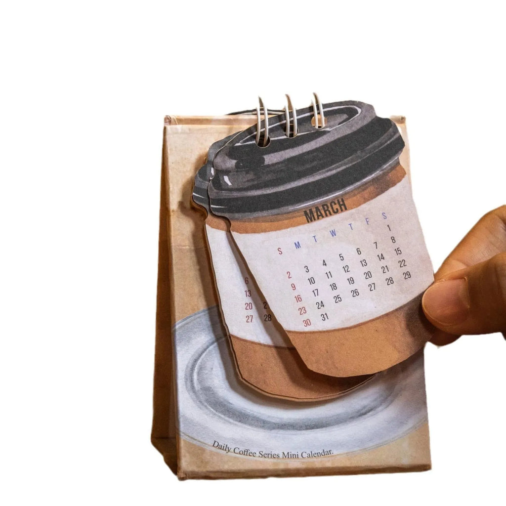 Small 2025 mini desk calendar open to a daily page, showing modern simple design on a desk.