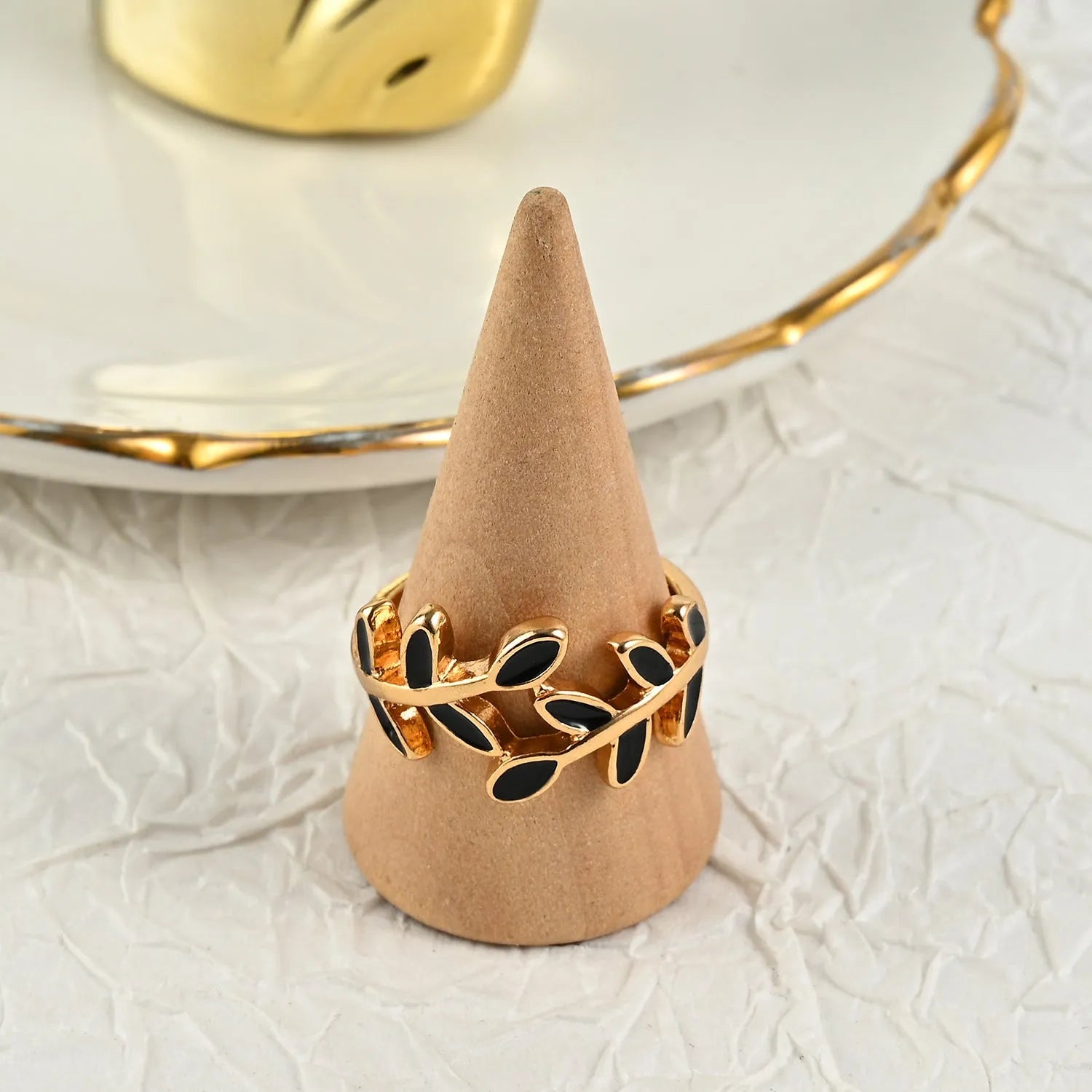 Gold-coloured acrylic ring with a geometric leaf and floral design on a white background.