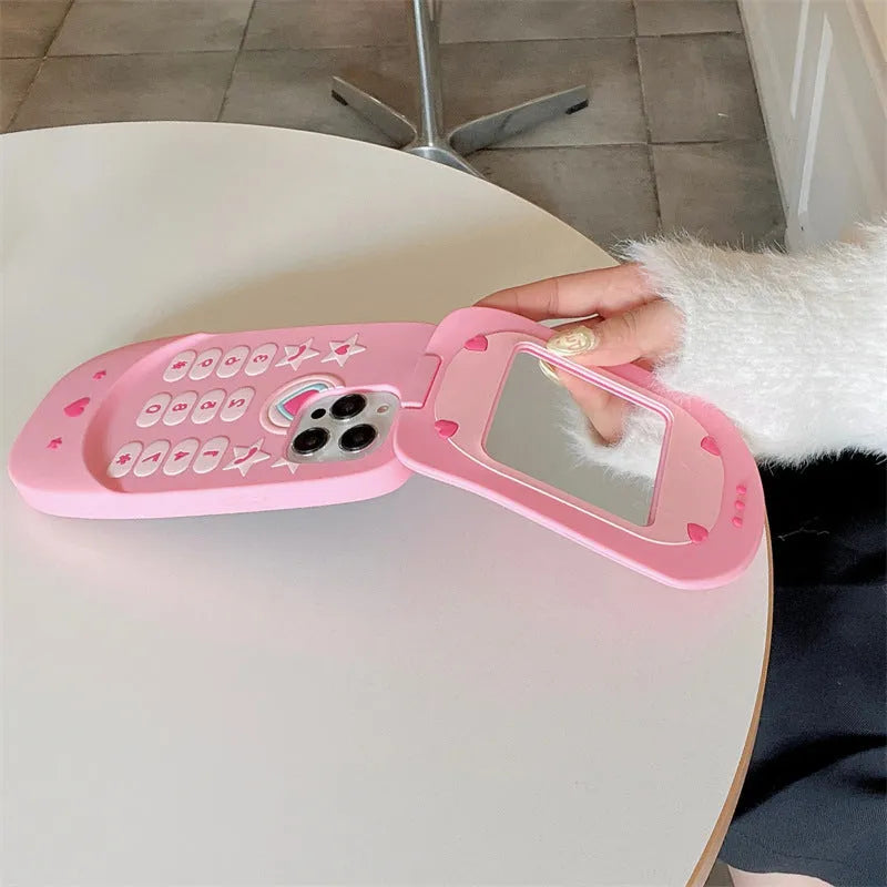 A light pink silicone iPhone case shaped like a flip phone with a built-in mirror on the front.