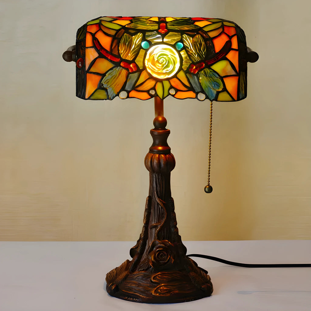 Tiffany-style desk lamp with coloured stained glass shade and resin base on a wooden desk.