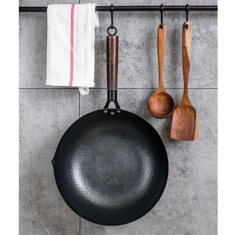 Handmade traditional black iron wok with a wooden handle, shown with a glass lid.