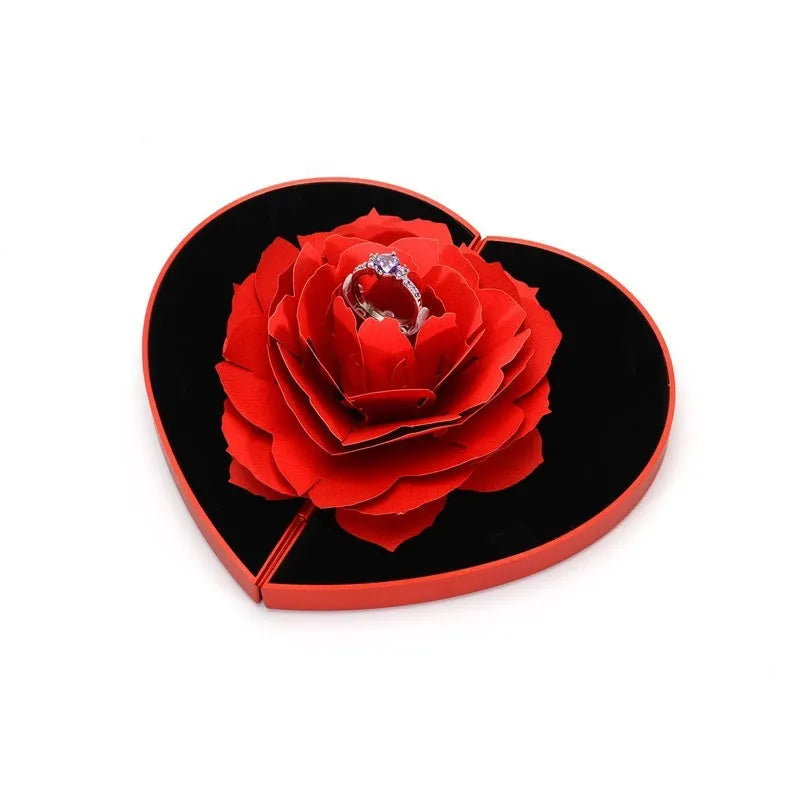 Red plastic heart-shaped rotating ring box with rose decoration inside white storage case