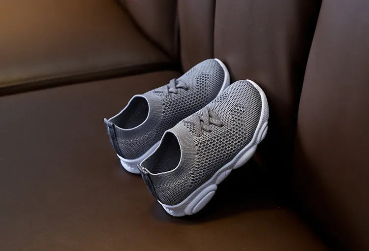 Children's white fabric lazy slip-on shoe with a non-slip rubber sole on a wooden floor.