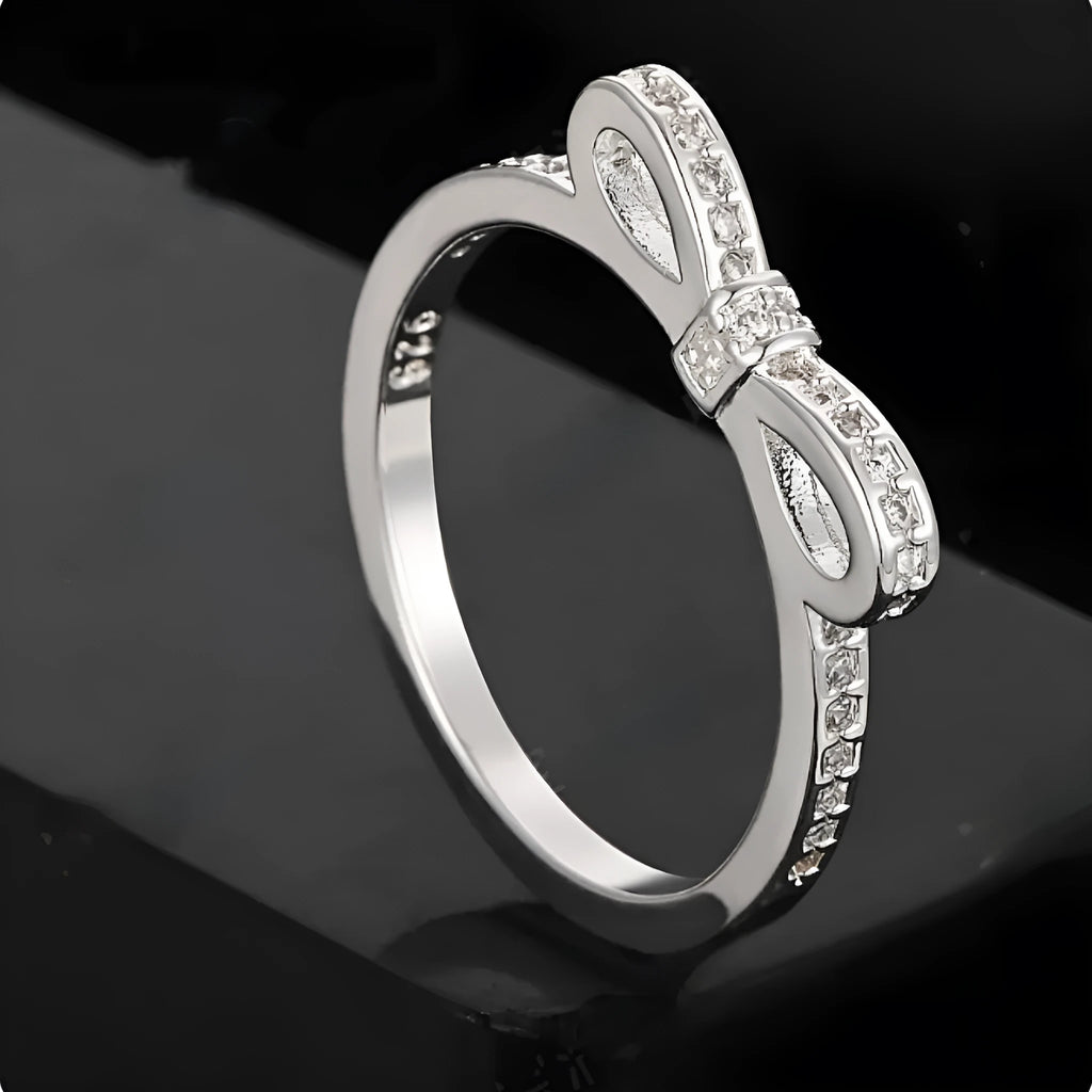 Silver coloured bow-shaped ring with sparkling rhinestone zircon crystals on a finger.