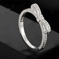 Silver coloured bow-shaped ring with sparkling rhinestone zircon crystals on a finger.