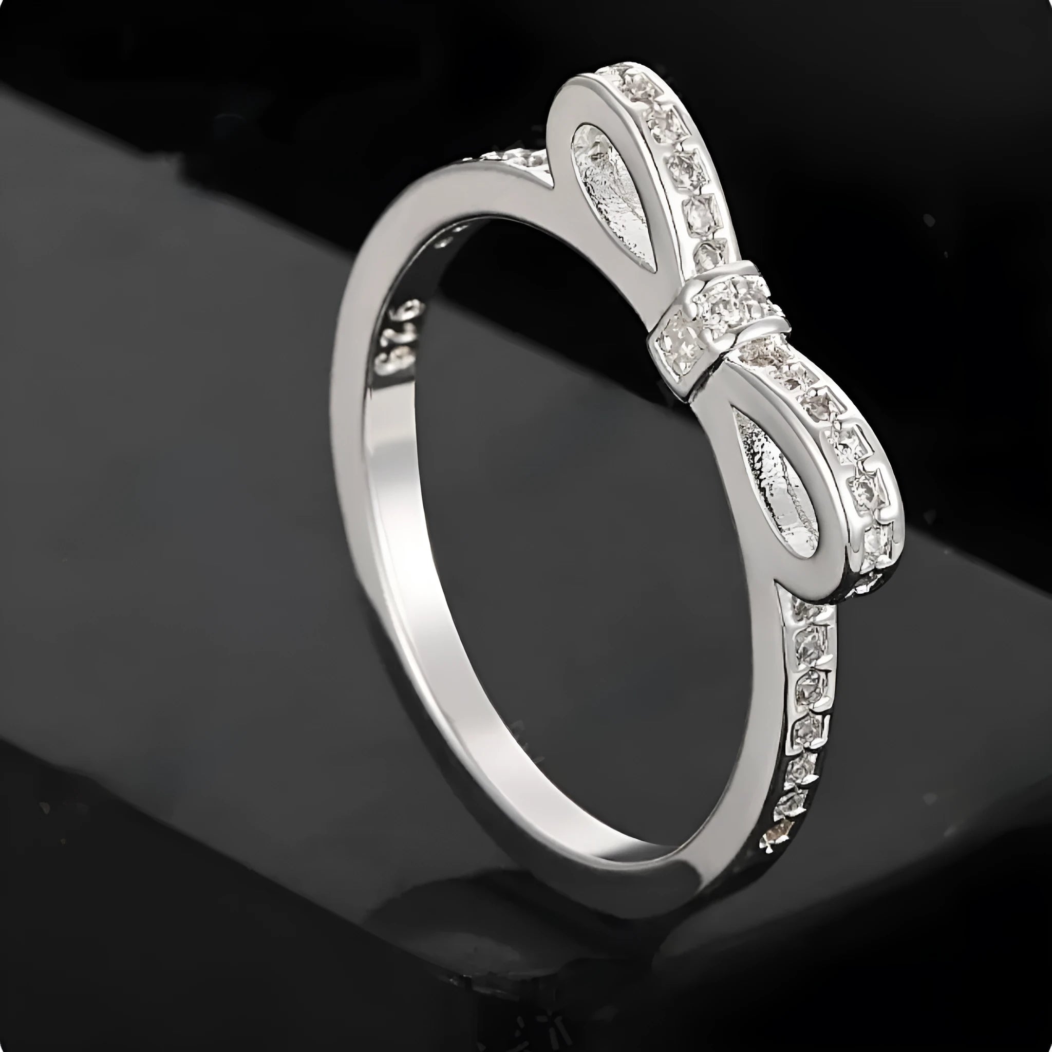 Silver coloured bow-shaped ring with sparkling rhinestone zircon crystals on a finger.