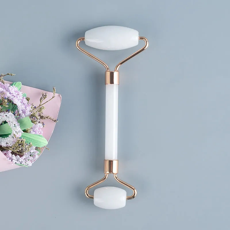 White jade facial roller with double heads and a matching gua sha scraping board on a plain surface.