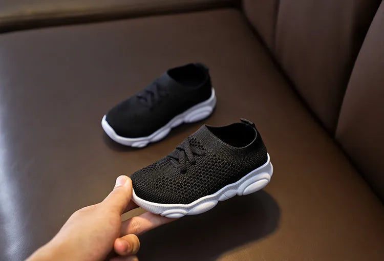 Children's white fabric lazy slip-on shoe with a non-slip rubber sole on a wooden floor.