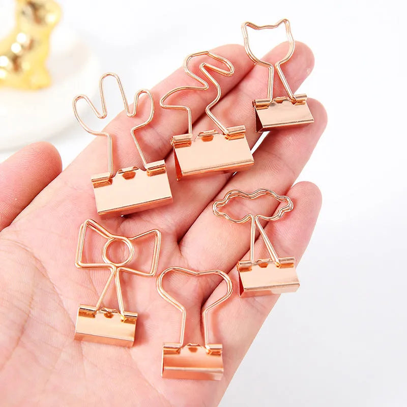 Gold metal clip with a decorative bow charm, shown holding papers.