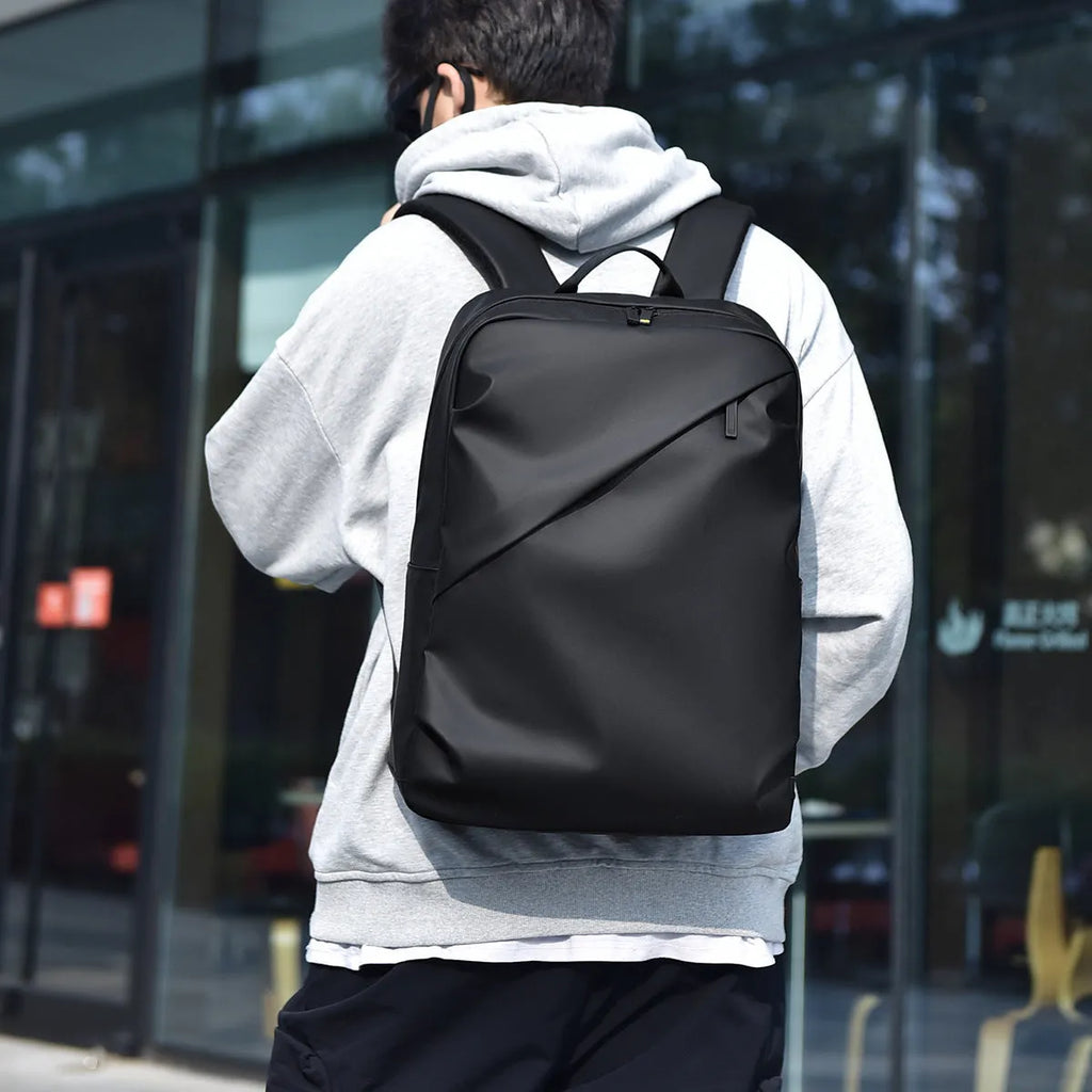 Men's large waterproof black PU leather backpack with laptop compartment on a grey background.