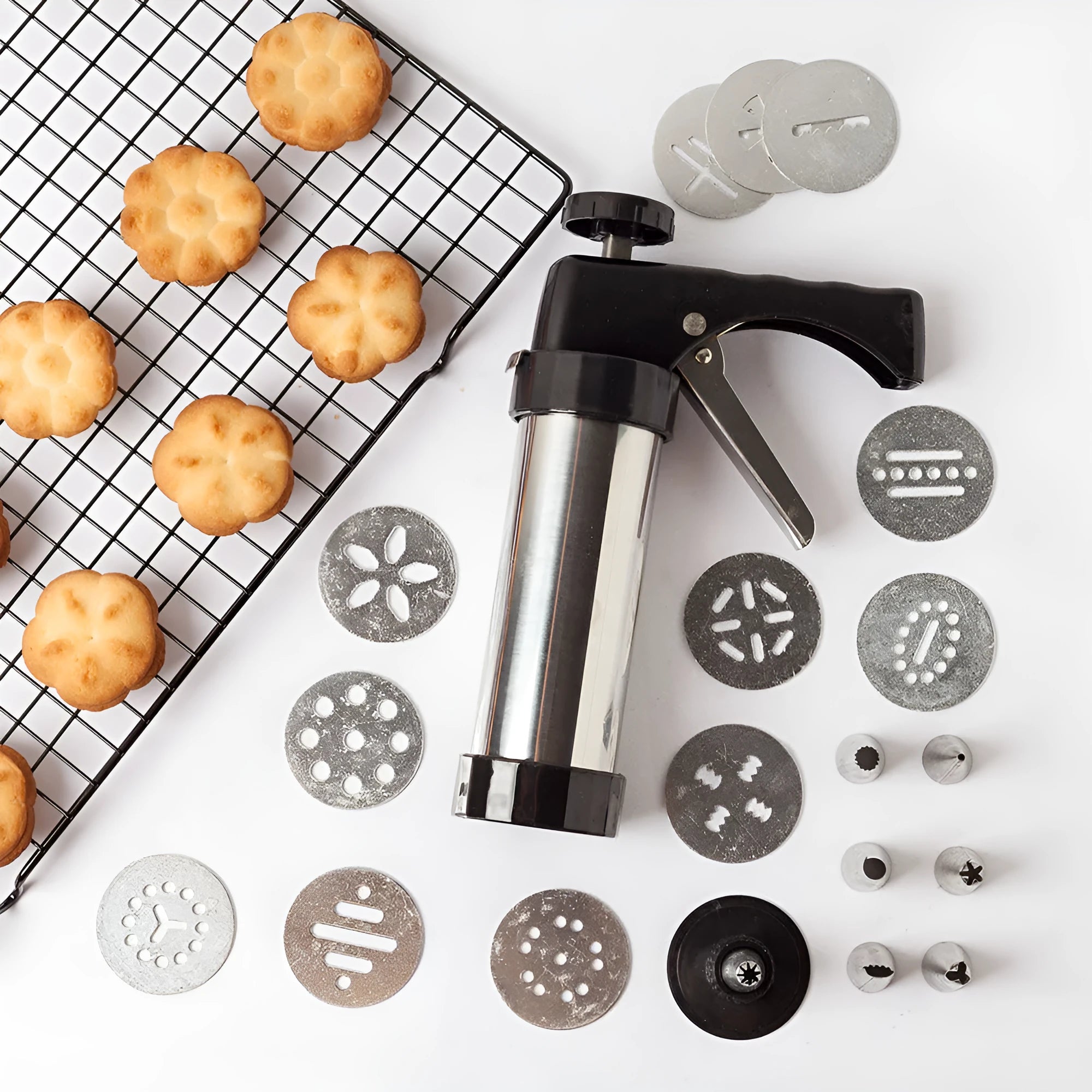 Stainless steel biscuit press machine with assortment of cookie moulds and piping nozzles on a kitchen worktop