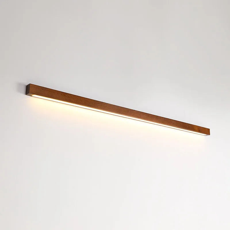Slim, long walnut-coloured wooden strip wall lamp mounted on a plain wall.
