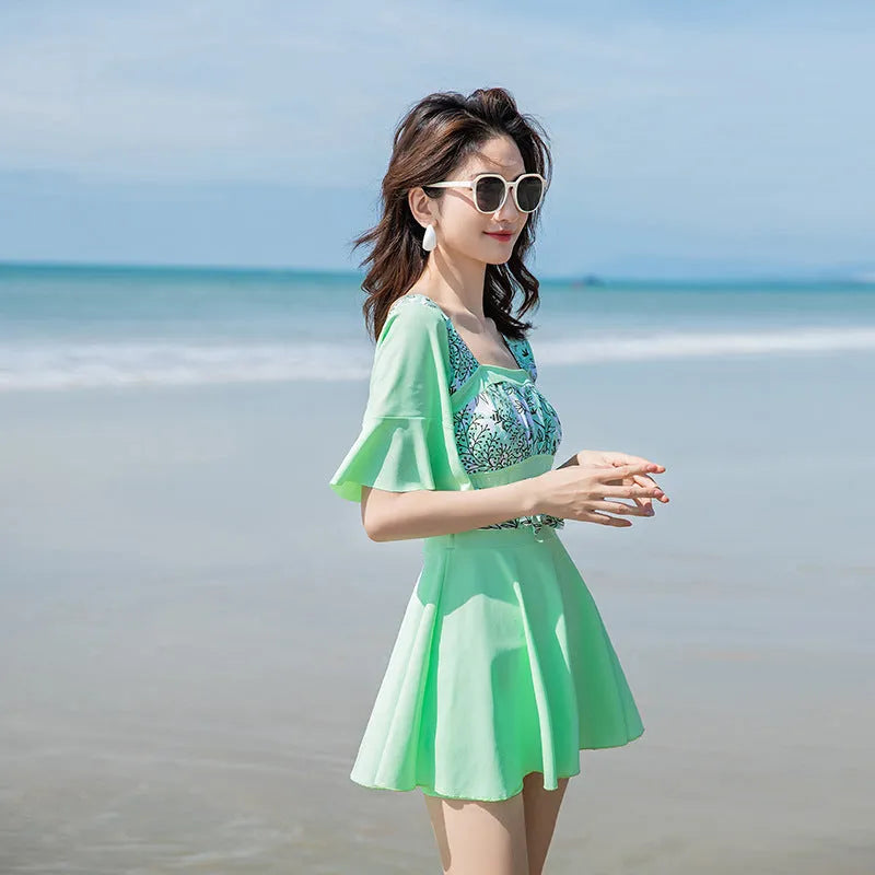 Green and blue women's one-piece swimsuit with a printed seaside pattern on a mannequin.