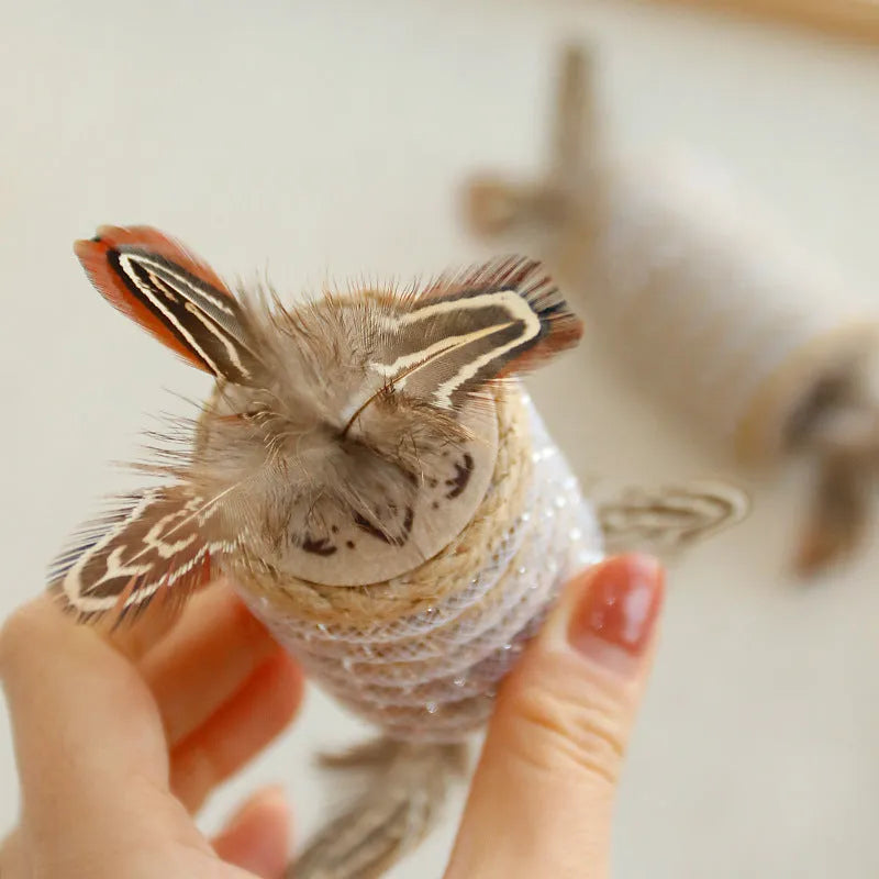 Beige cat toy with feathers, hemp rope scratching area and a central sound roller for pet claw play.