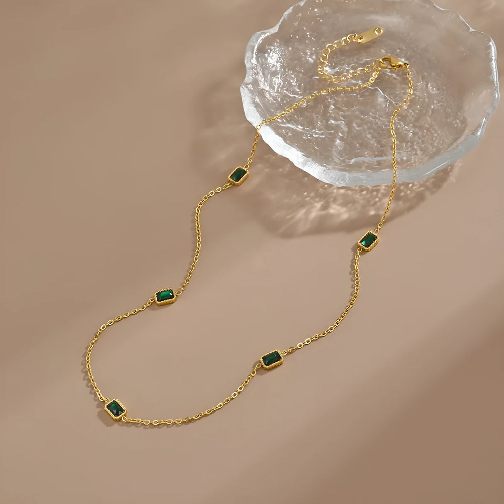Titanium steel emerald zircon necklace and bracelet set with gold hardware and O-ring chain on a white background