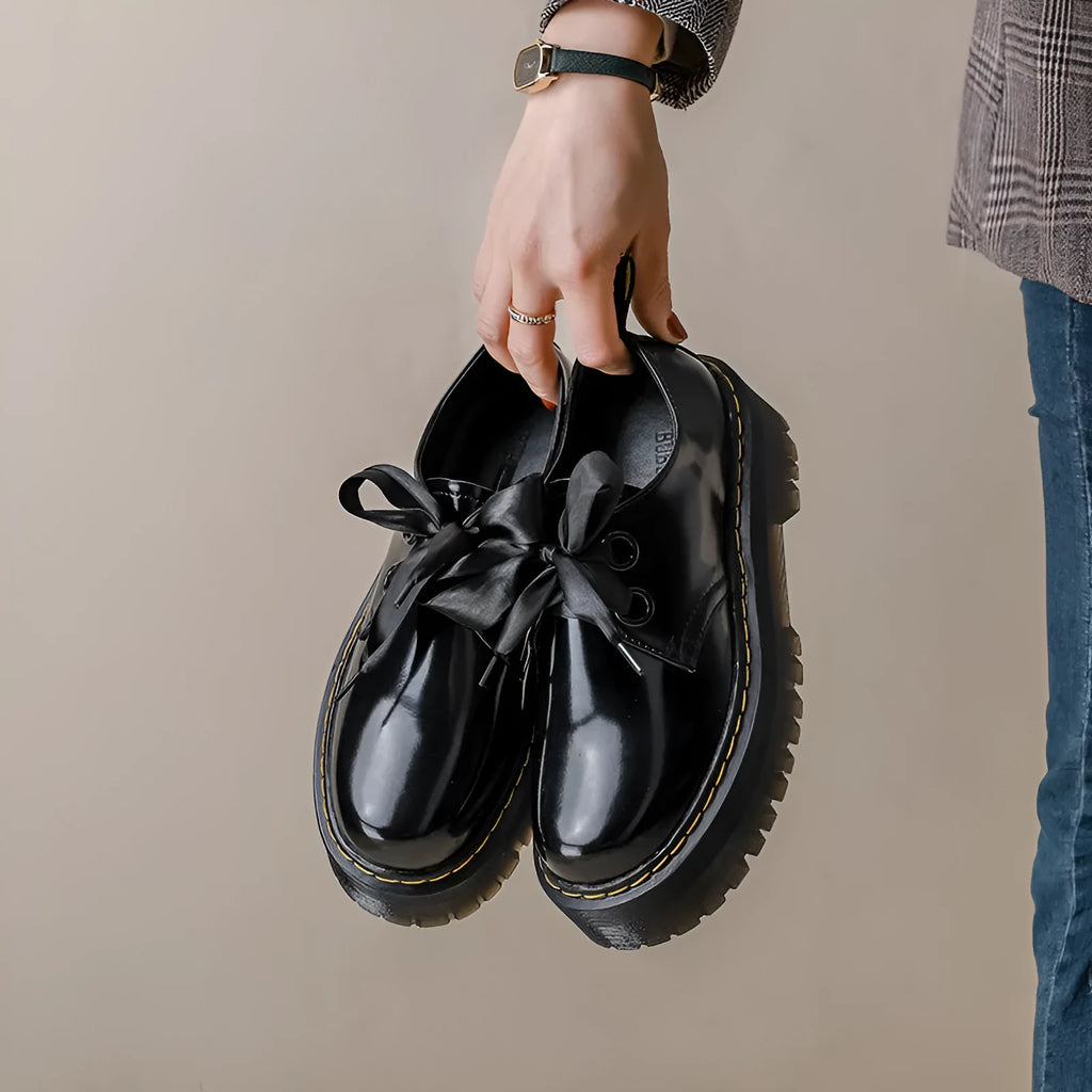 Black women's lace-up shoes with a thick sole, ribbon detail, and cross straps.