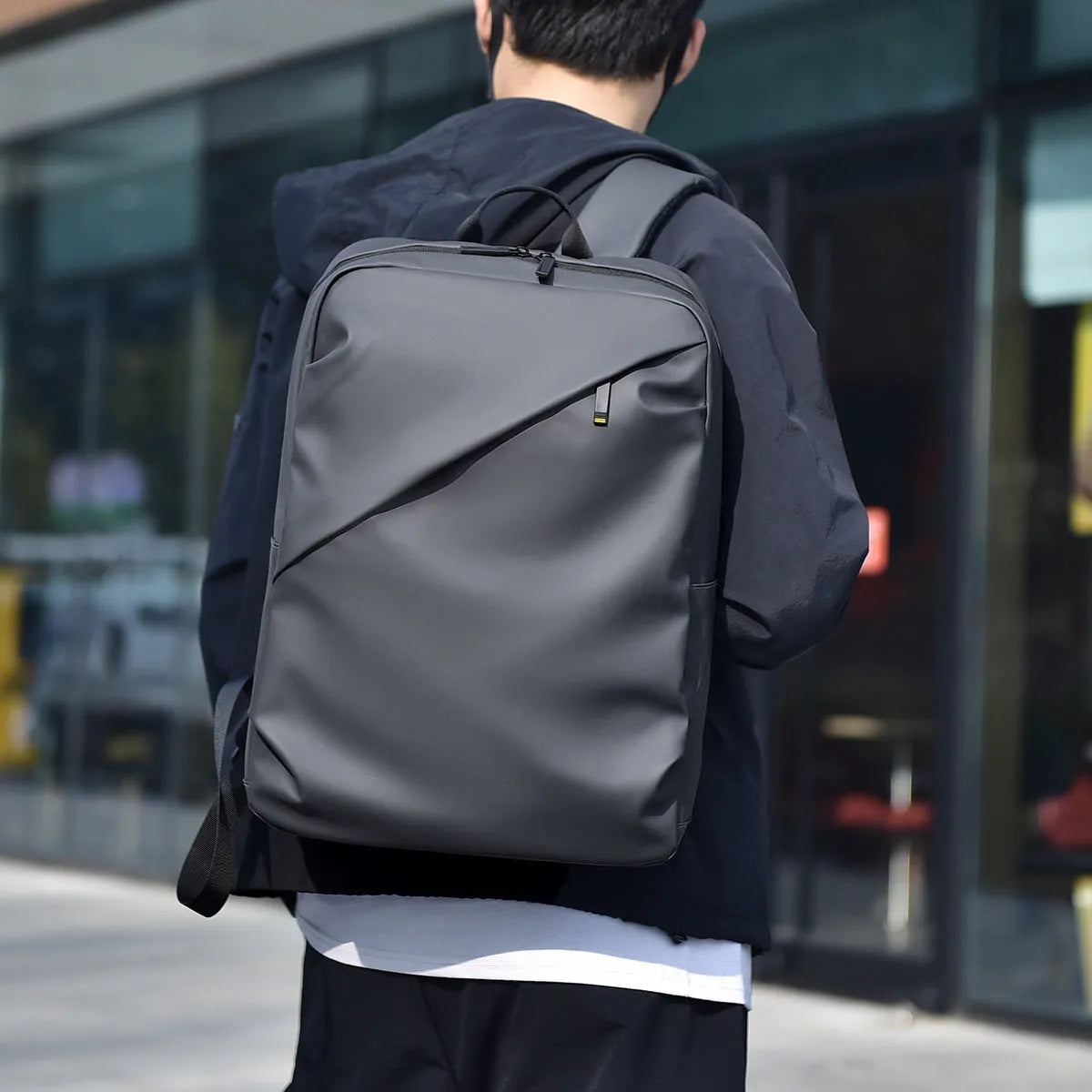 Men's large waterproof black PU leather backpack with laptop compartment on a grey background.