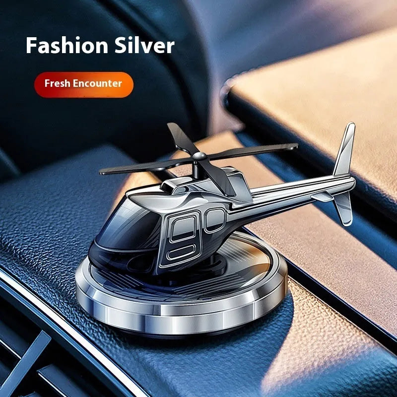 Silver solar-powered metal helicopter car air freshener ornament with spinning blades on a dashboard.