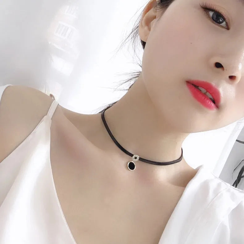Women's short black clavicle necklace with round gold alloy pendant and leather rope chain on display
