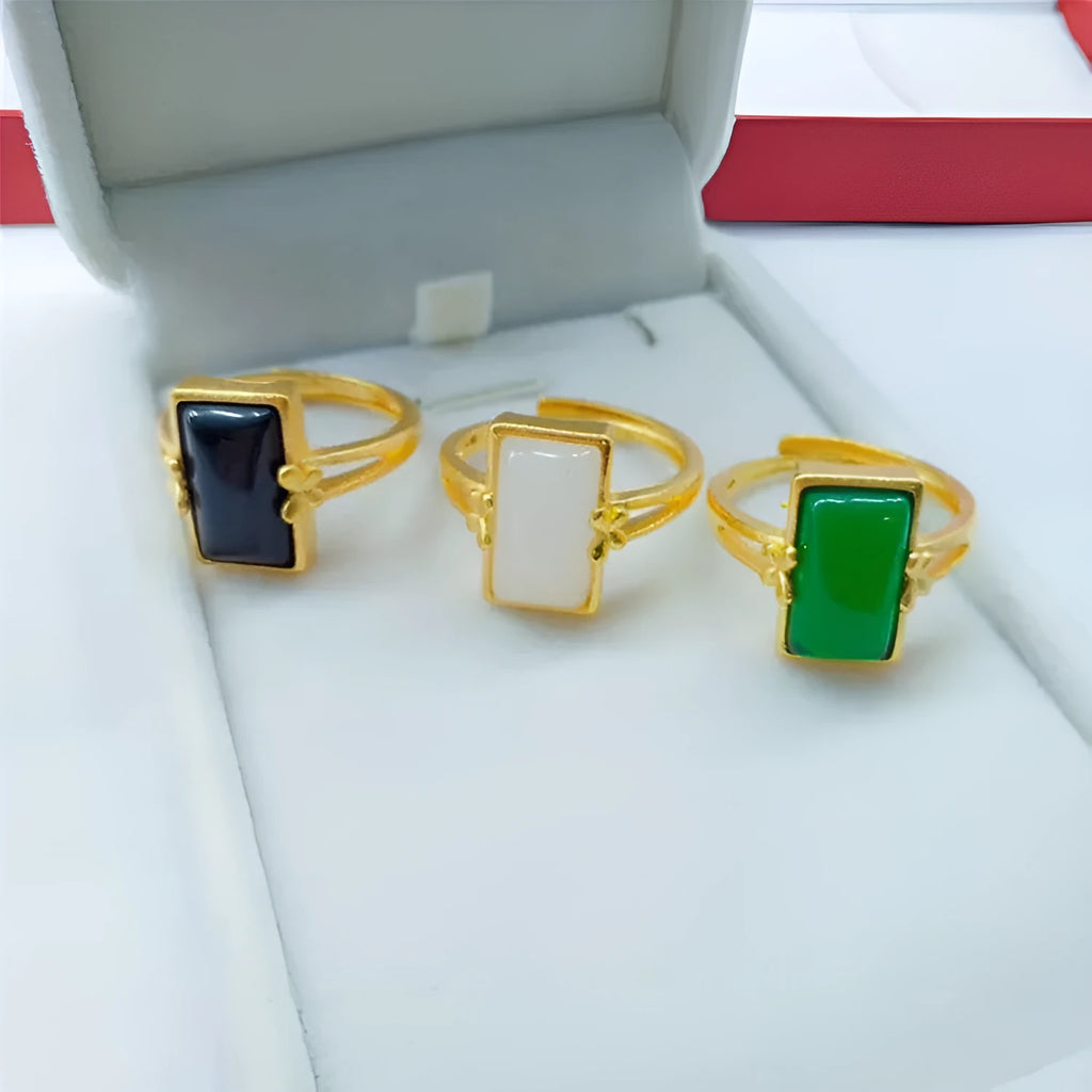 Adjustable gold-plated brass ring with a black artificial gemstone on a neutral background.