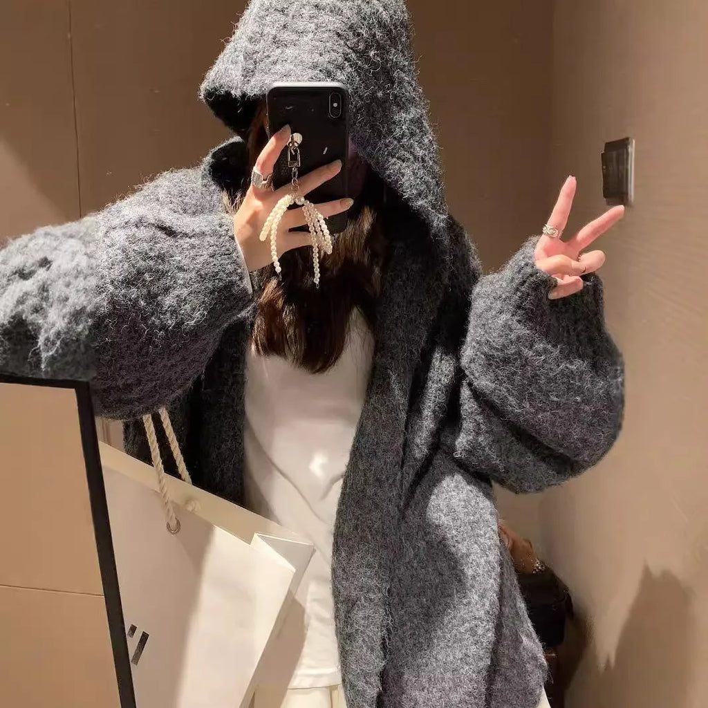 A woman wearing a thick, loose-fit, dark grey hooded sweater cardigan with a retro design.
