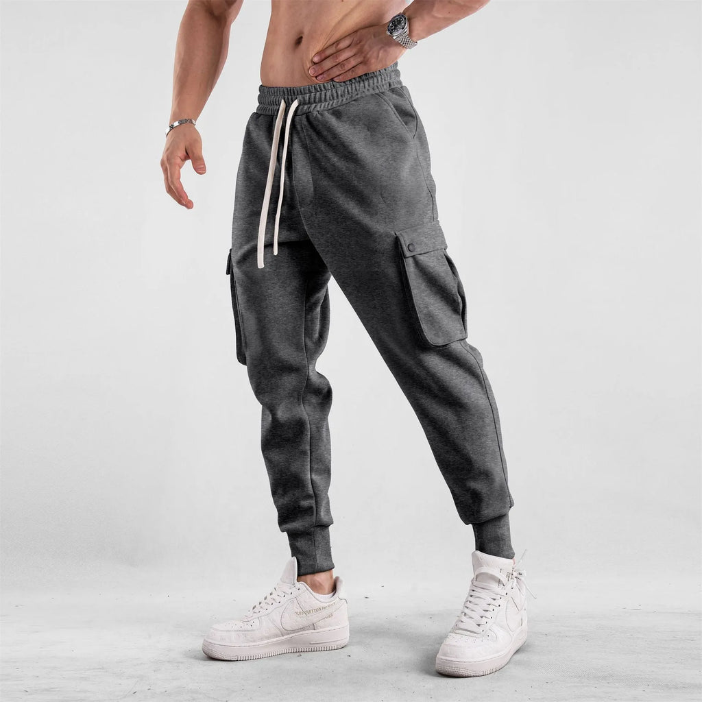 Men's loose light grey cotton trousers with ankle ties and multiple pockets laid flat.
