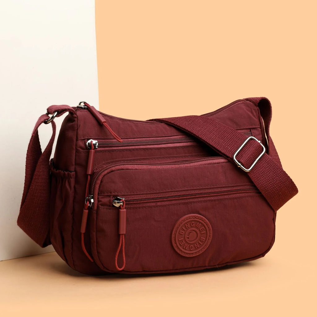 Grey water-repellent nylon crossbody bag showing front three-dimensional pocket and adjustable shoulder strap.