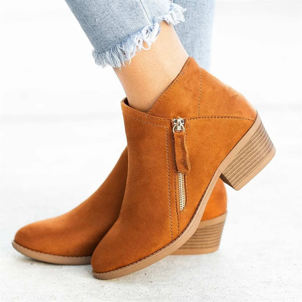 Women's beige suede ankle boots with a side zip and chunky heel on a plain background.